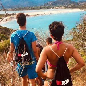 Un gruppo WeRoad, visto da dietro, si erge su una collina che si affaccia su una spiaggia affollata con acqua turchese brillante.