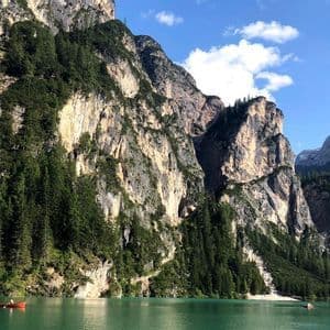 Eine WeRoad Gruppenreise mit Kanus auf einem türkisfarbenen See am Fuße großer, bewaldeter Berge unter blauem Himmel.