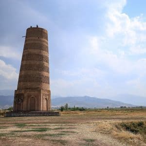 Un alto minareto in mattoni si erge in un vasto paesaggio arido, con due persone in cima e montagne all'orizzonte.