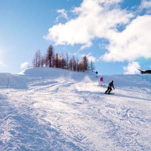 Eine WeRoad Gruppenreise zum Skifahren und Snowboarden auf einem verschneiten Berghang an einem sonnigen Tag bei strahlend blauem Himmel.