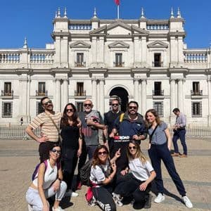 Un groupe WeRoad pose pour une photo sur une place ensoleillée, devant un grand bâtiment classique avec un drapeau.
