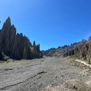 A wide, rocky canyon floor flanked by tall, spiky rock formations under a clear blue sky.