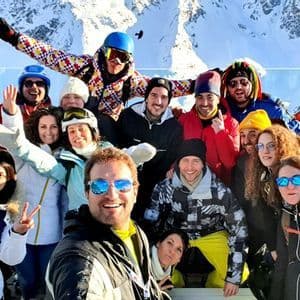 Un gruppo WeRoad in viaggio, con indosso l'attrezzatura da sci invernale, si scatta un selfie di gruppo in una giornata di sole, con montagne innevate sullo sfondo.