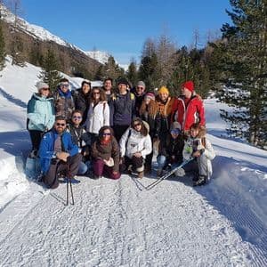 Un gruppo WeRoad in viaggio posa per una foto su un sentiero in una valle di montagna innevata, circondata da pini, sotto un cielo azzurro e limpido.