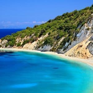 Una caletta appartata con acqua turchese cristallina e una spiaggia di sabbia bianca, incastonata tra verdi scogliere alberate sotto un cielo azzurro.