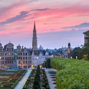 Une vue panoramique sur un jardin à la française vers l'horizon d'une ville européenne historique avec une haute flèche sous un coucher de soleil rose éclatant.