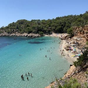 Una vista dall'alto di una caletta affollata con persone che nuotano in acqua limpida e turchese e prendono il sole sulla sabbia.