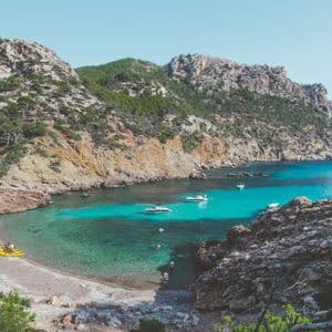 Eine Luftaufnahme einer abgelegenen Bucht mit klarem türkisfarbenem Wasser, wo mehrere Boote nahe einem Kieselstrand ankern.