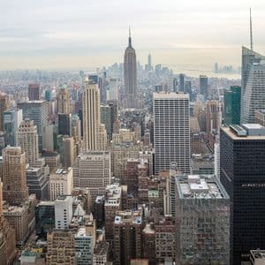 Una veduta aerea di un denso skyline urbano con numerosi grattacieli, tra cui l'Empire State Building, sotto un cielo coperto.