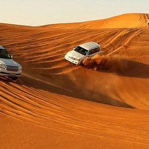 Tre SUV bianchi attraversano dune di sabbia arancioni ondulate durante un safari nel deserto di un viaggio di gruppo WeRoad.