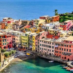 Vista panorámica de un pueblo costero con edificios coloridos, apiñados en un acantilado que domina un puerto turquesa y el mar azul.
