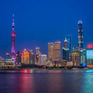 Uno skyline cittadino moderno di notte, con edifici illuminati e un'alta torre che si riflette sull'acqua calma.