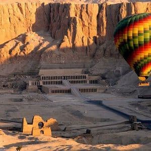 Una mongolfiera colorata galleggia su un antico complesso di templi alla base di scogliere illuminate dal sole nel deserto.