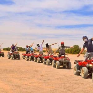 Un viaggio di gruppo WeRoad con le braccia aperte in posa su una fila di quad rossi in un paesaggio desertico.