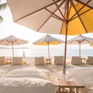 Sotto un grande ombrellone giallo e bianco, delle poltrone a sacco sono posizionate su una spiaggia sabbiosa di fronte al mare all'alba.