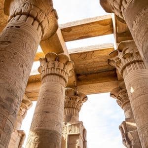 Una vista dal basso di grandi colonne di pietra con geroglifici scolpiti all'interno di un antico tempio, che sorreggono un soffitto di pietra.