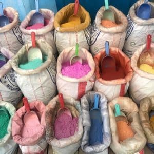 A collection of open white sacks filled with brightly colored powdered pigments, each with a plastic scoop inside.