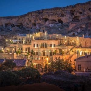 Edifici in pietra illuminati e abitazioni rupestri incastonate in un fianco roccioso al crepuscolo.