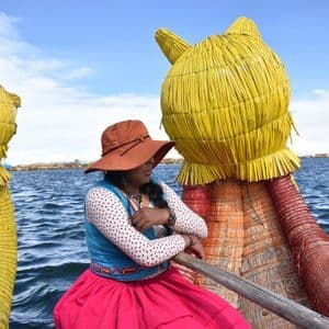 Una donna in abiti tradizionali colorati siede su una barca di giunco decorata su un grande lago sotto un cielo parzialmente nuvoloso.