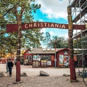 Der Eingang zu Christiania ist durch ein großes rotes Schild gekennzeichnet, das von zwei hohen, geschnitzten hölzernen Totempfählen mit Gesichtern gehalten wird.