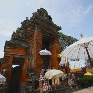 A low-angle view of an ornate, multi-tiered brick temple entrance decorated with traditional white and yellow umbrellas.