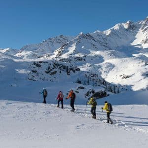 Un viaggio di gruppo WeRoad con ciaspolata in fila indiana, circondati da montagne innevate sotto un cielo sereno.