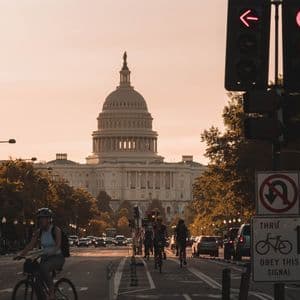 Cyclists ride down a city street with the U.S. Capitol Building in the background during a golden sunset.