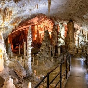 Un sentiero pavimentato si snoda attraverso una grande grotta piena di stalattiti e stalagmiti illuminate.