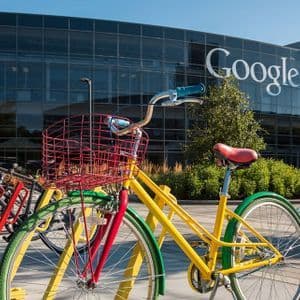 Biciclette colorate parcheggiate in una rastrelliera davanti alla moderna sede in vetro di Google in una giornata di sole.