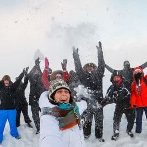 Eine Frau macht ein Selfie mit ihrer WeRoad-Gruppe, während sie in einer weiten, verschneiten Landschaft jubeln und Schnee werfen.