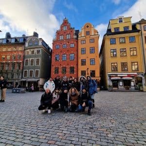 Eine WeRoad-Gruppenreise posiert für ein Foto auf einem Kopfsteinpflasterplatz vor farbenfrohen historischen Gebäuden.