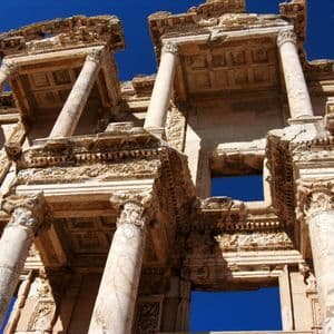 A low-angle view of the ornate stone facade of an ancient ruin with columns, set against a deep blue sky.