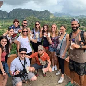 Un gruppo WeRoad in posa per una foto con bevande su un punto panoramico che si affaccia su una lussureggiante valle verde e le montagne.