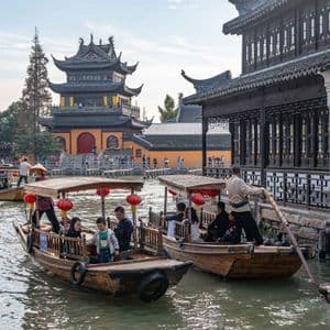 Persone su barche di legno percorrono un canale fiancheggiando edifici tradizionali e una grande pagoda.