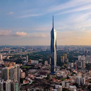 Eine Luftaufnahme eines modernen, geometrischen Wolkenkratzers mit einem hohen Turm, der sich bei Sonnenuntergang über einer dichten Stadtlandschaft erhebt.