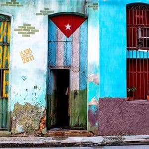 Una pared colorida y desgastada con una puerta pintada con la bandera cubana, una puerta enrejada verde y amarilla, y una ventana enrejada roja.