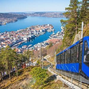 Una funicolare blu sale su un binario su un pendio soleggiato, offrendo una vista panoramica di una città costiera e del suo porto sottostante.