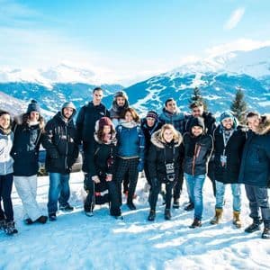 Eine WeRoad-Gruppenreise posiert für ein Foto auf einem verschneiten Berg mit Panoramablick auf weitere Gipfel.