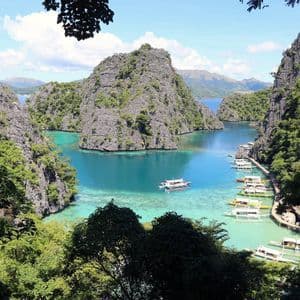 Una vista dall'alto di una laguna tropicale con acqua turchese, circondata da ripide scogliere ricoperte di giungla e piena di barche a bilanciere.