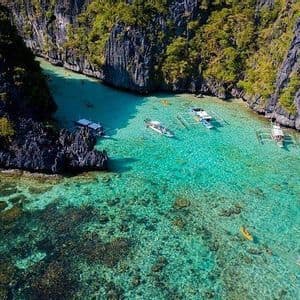 Vista aerea di barche e kayak di un viaggio di gruppo WeRoad in una limpida laguna turchese circondata da scogliere rocciose e verdi.