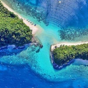 Vista aerea di due isole ricoperte da fitta foresta verde, collegate da un istmo di sabbia in acque cristalline turchesi.