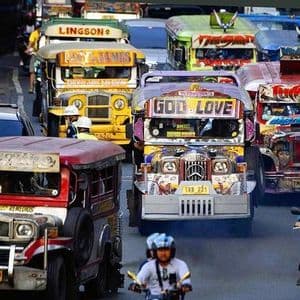 Diversi Jeepney colorati e motociclette percorrono una strada trafficata della città in mezzo al traffico intenso di giorno.