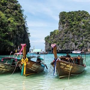 Barche tradizionali in legno a coda lunga, adornate con nastri colorati, ormeggiate in acque turchesi in una baia circondata da lussureggianti scogliere rocciose.
