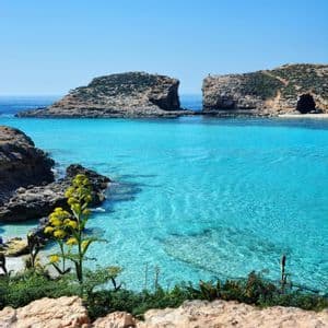 A rocky bay with clear, shallow turquoise water surrounded by cliffs under a sunny, clear sky.