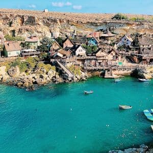 A colorful village built into a rocky cliffside, overlooking a small bay with turquoise water and several boats.