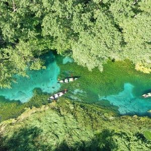 Vista aerea di un viaggio di gruppo WeRoad in kayak su un fiume limpido e turchese attraverso una foresta verde lussureggiante