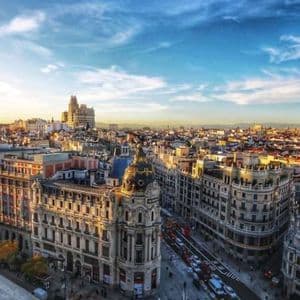 Una vista panoramica di un paesaggio urbano europeo al tramonto, con luce dorata che illumina gli edifici e un cielo blu parzialmente nuvoloso.
