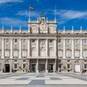 La grandiosa facciata di un palazzo storico si erge dietro una grande piazza pavimentata sotto un cielo azzurro limpido