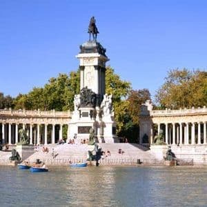 Un grande monumento con una statua equestre in cima si erge sulla riva di un lago con persone in barche a remi.