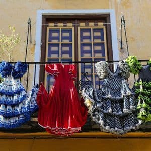 Quattro abiti da flamenco colorati con balze appesi a uno stendibiancheria su un balcone di fronte a una finestra.